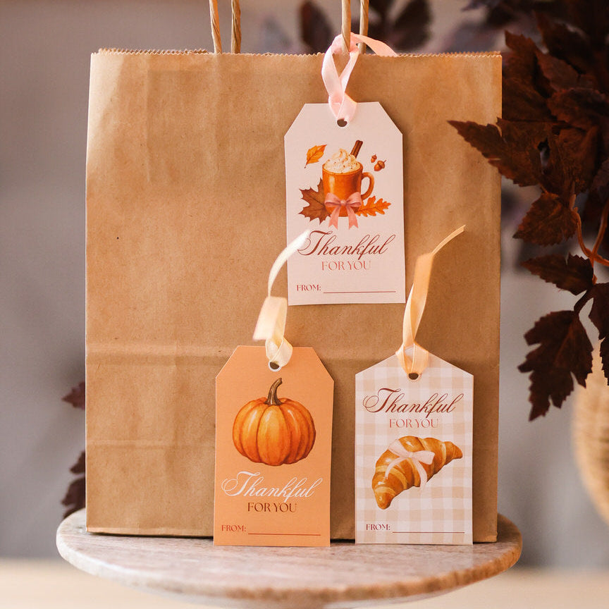 Brown paper bag with 'Thankful' tags on a wooden stand with pumpkins and a candle.